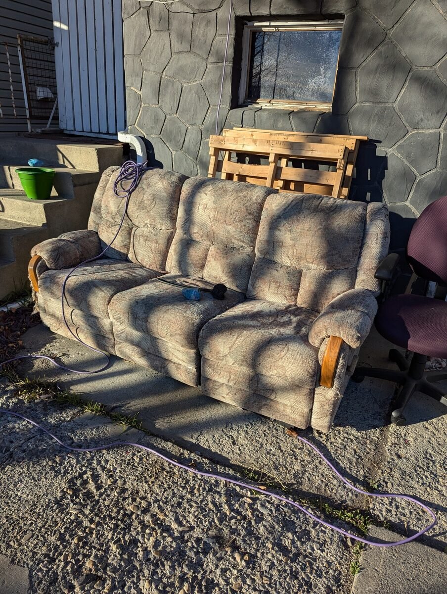 An old sofa carried out and set by the fence for haul-away during a Clearout Crew furniture removal in the Calgary area.
